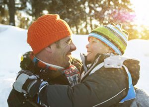 A father and son smiling at each other in the snow, free of dental anxiety.
